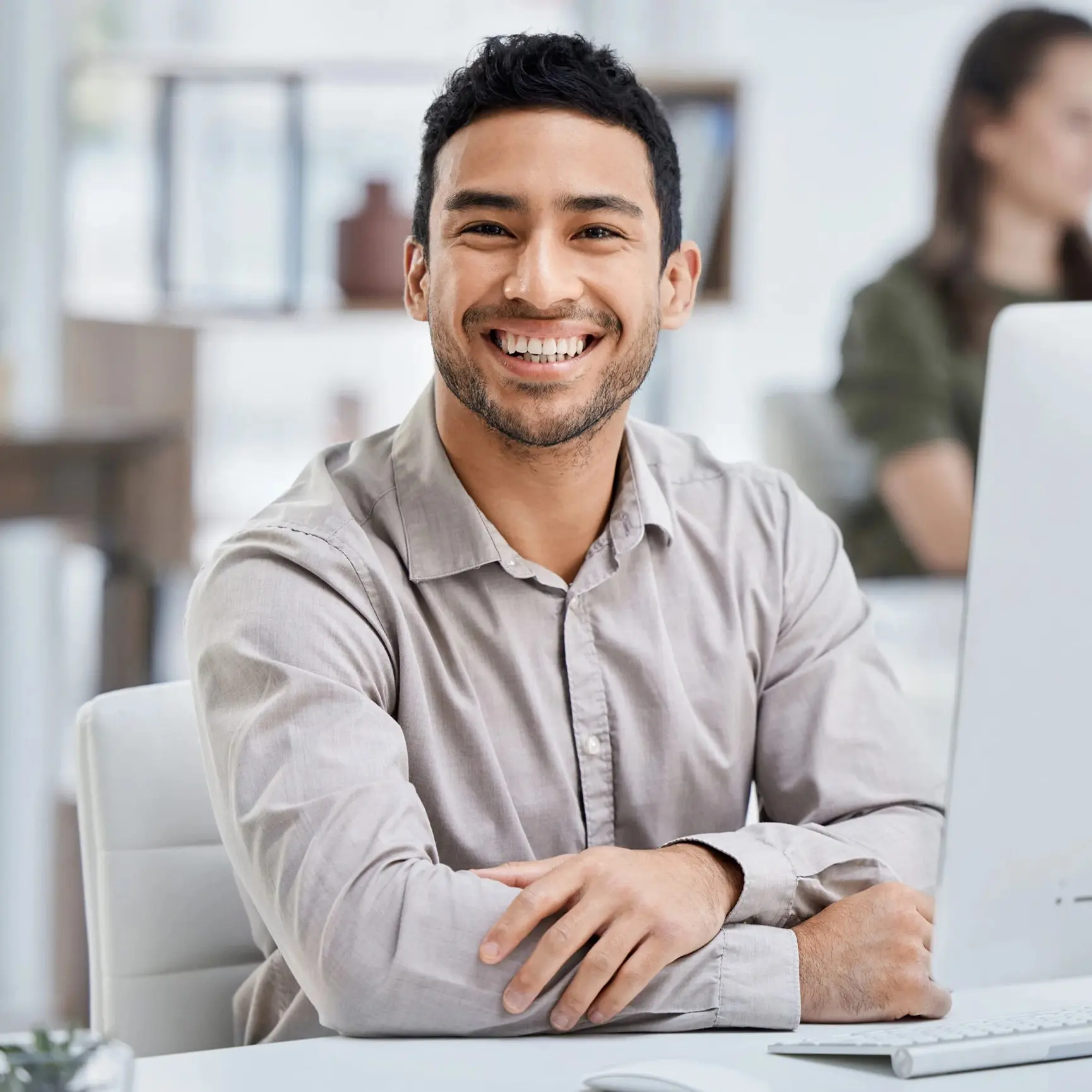Smiling young businessman sitting at a desk with a computer in a modern office environment.